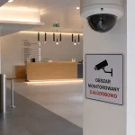 Kamera kopułkowa CCTV oraz tabliczka informacyjna o monitoringu całodobowym przy wejściu do biurowca